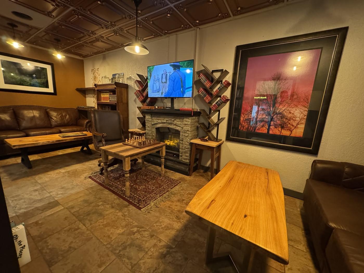 The sitting room at Magnolia Market: leather sofas, live-edge wood tables, a stone fireplace, a chess set left mid-game and shelves of books under a pressed tin ceiling.
